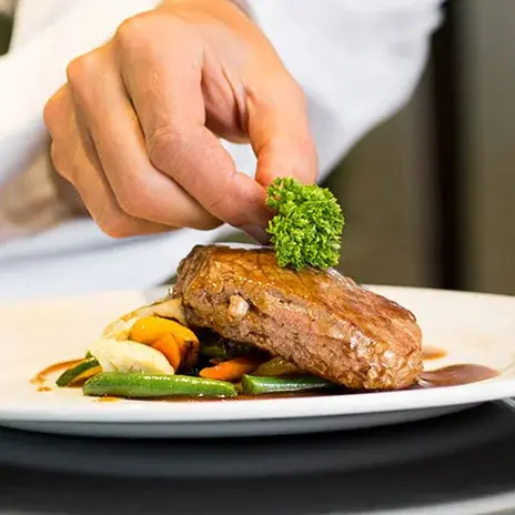 [[community_name]] Chef Created Meals, chef garnishing a plate.